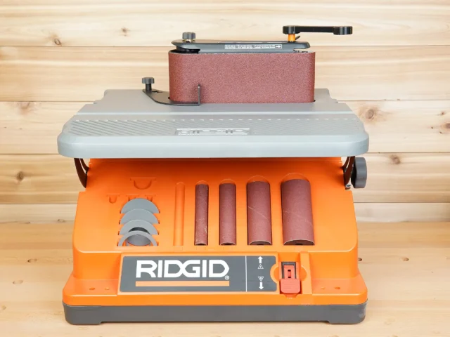 Ridgid oscillating edge sander with wrench-style tool positioned over front adjustment knob, showing sanding drums and belt below
