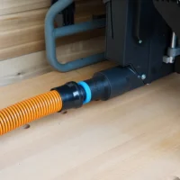 Black 1-1/4 inch hose adapter with blue ring joining an orange shop vac hose to a Craftsman table saw dust port