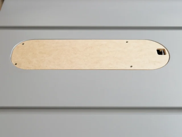 Light wood MDF zero clearance insert with rounded ends, four mounting holes, and a rectangular opening, positioned flat on a gray surface