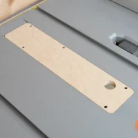 Light wood MDF zero clearance insert with rounded corners and three mounting holes, positioned in gray Ridgid table saw throat