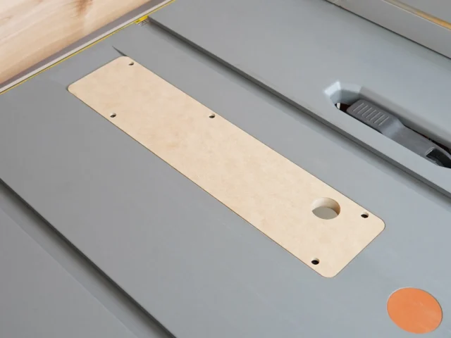 Light wood MDF zero clearance insert with rounded corners and three mounting holes, positioned in gray Ridgid table saw throat