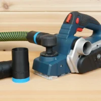Black ToolCurve hose adapter with blue collar lying beside a Bosch PL2632 planer and green vac hose