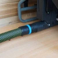 Black ToolCurve hose adapter with blue ring joining a green braided vacuum hose to a Craftsman table saw dust port