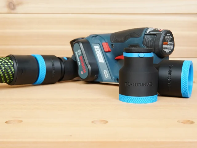 Black 36mm ToolCurve hose adapter with blue knurled ring standing beside a Bosch 12V MAX planer and hose