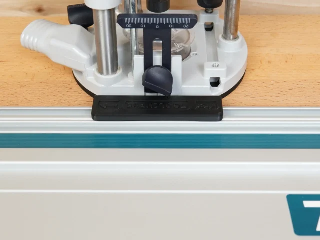 Guide rail adapter for Festool OF 1010 router mounted on a track saw rail, showing the white base with black knob and measurement scale