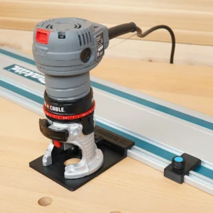 Black ToolCurve rail adapter base under a Porter Cable trim router, riding a Makita guide rail on wood