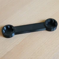 Black 3D-printed wrench with circular sockets at each end, laid flat on wood surface
