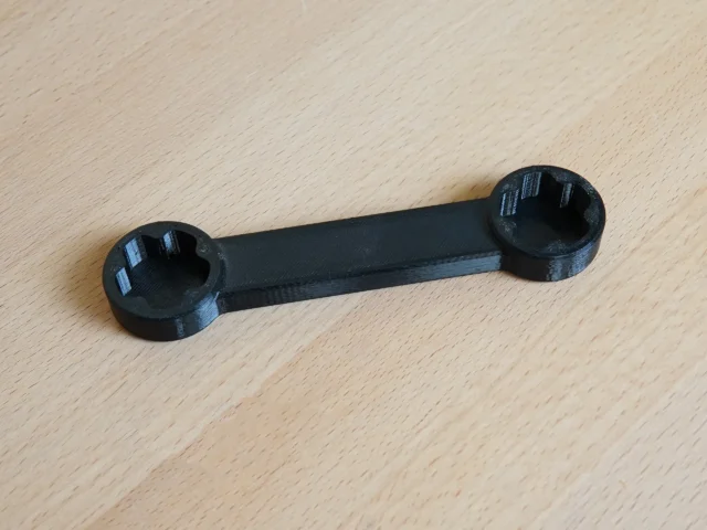 Black 3D-printed wrench with circular sockets at each end, laid flat on wood surface