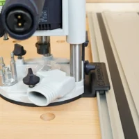 Guide rail adapter for Festool OF 1010 router mounted on track saw rail, showing white base with threaded holes and dust extraction port