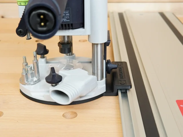 Guide rail adapter for Festool OF 1010 router mounted on track saw rail, showing white base with threaded holes and dust extraction port