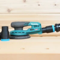 Black and blue 1-1/4 inch ToolCurve hose adapter shown loose beside a Makita XGT sander with a second adapter joining its dust port to an orange hose