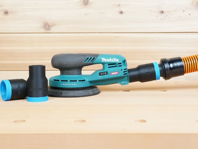 Black and blue 1-1/4 inch ToolCurve hose adapter shown loose beside a Makita XGT sander with a second adapter joining its dust port to an orange hose