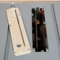 Cream-colored MDF zero clearance insert for Ridgid R4513 table saw, shown next to the original metal insert for comparison
