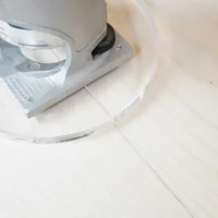 6" round clear acrylic router base plate mounted on a Bosch Colt trim router, shown from above on a light wood surface