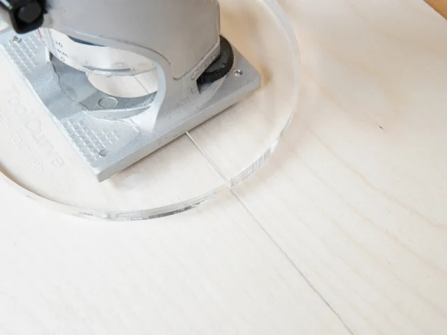 6" round clear acrylic router base plate mounted on a Bosch Colt trim router, shown from above on a light wood surface