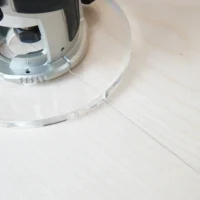 6" clear acrylic router base plate mounted on a Makita trim router, shown from above on a wooden surface