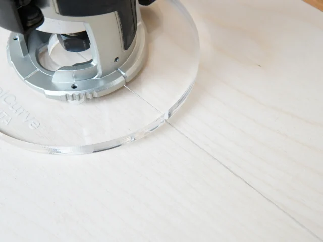 6" clear acrylic router base plate mounted on a Makita trim router, shown from above on a wooden surface