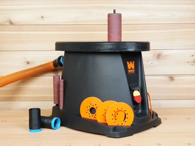 Black 1-1/4 inch hose adapter with blue ring beside a WEN oscillating spindle sander, orange hose attached