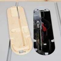Zero clearance insert for SawStop table saw shown from above, cream-colored MDF base on left with mounting holes and adjustment slots, metallic insert mechanism on right with red adjustment knob and stainless offset screws