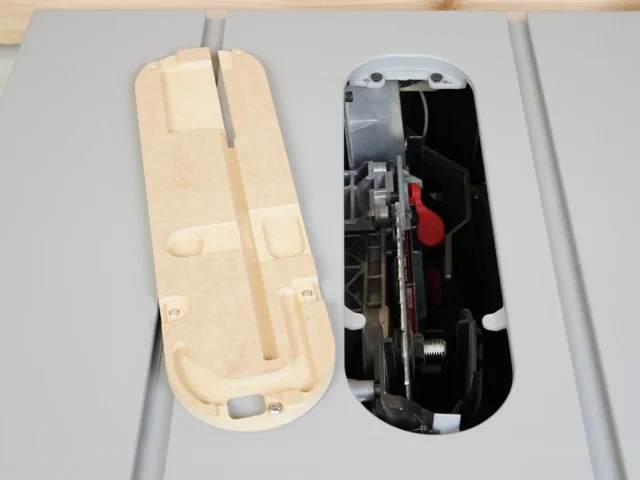 Zero clearance insert for SawStop table saw shown from above, cream-colored MDF base on left with mounting holes and adjustment slots, metallic insert mechanism on right with red adjustment knob and stainless offset screws