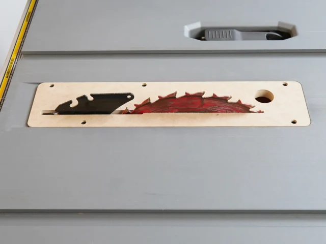 Light wood zero clearance insert for Ridgid table saw, showing black and red saw blade profiles cut through the center, mounted on saw table