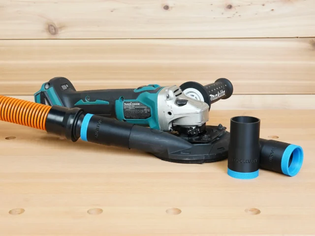 Black 1-1/4 inch hose adapter with blue trim linking an orange hose to a Makita grinding shroud, two spare adapters beside it