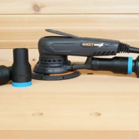 Black ToolCurve 1-1/4 inch hose adapter with blue ring lying beside a MAXXT sander, second adapter fitted to its dust port