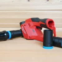 Black 1-1/4 inch hose adapter with blue band linking an orange vac hose to a Milwaukee M12 planer, two spares beside