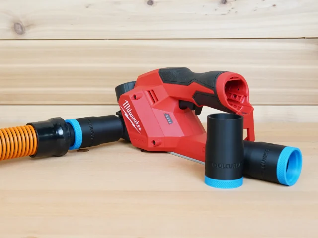 Black 1-1/4 inch hose adapter with blue band linking an orange vac hose to a Milwaukee M12 planer, two spares beside