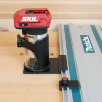 SKIL 20v trim router mounted to Makita guide rail via black adapter base on wooden workbench