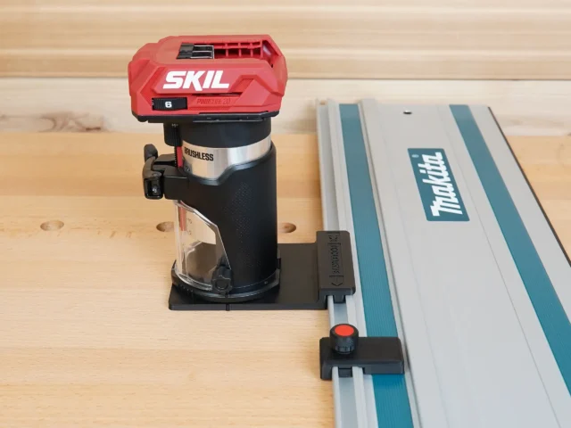 SKIL 20v trim router mounted to Makita guide rail via black adapter base on wooden workbench