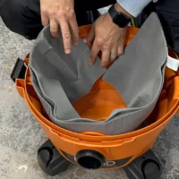 Gray polyester reusable dust bag with elastic top opening, shown installed in an orange Ridgid or Craftsman shop-vac, held open to display interior