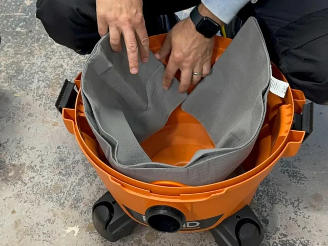 Gray polyester reusable dust bag with elastic top opening, shown installed in an orange Ridgid or Craftsman shop-vac, held open to display interior