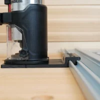 Black plastic guide rail adapter mounted on a SKIL trim router, positioned on a track saw rail over a wooden workbench