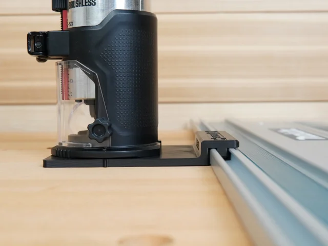 Black plastic guide rail adapter mounted on a SKIL trim router, positioned on a track saw rail over a wooden workbench