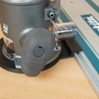 Gray 3D-printed guide rail adapter mounted on a Ridgid 2 HP router base, shown attached to a Makita guide rail