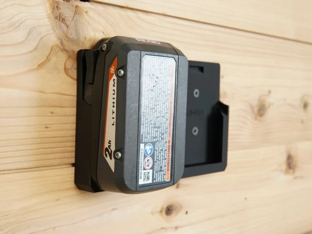 Black plastic battery mount holding a Ridgid 18v lithium-ion battery on a wooden wall