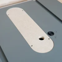 Cream-colored MDF zero clearance insert for Hercules table saw, mounted in gray table surface with center blade opening and adjustment screw holes