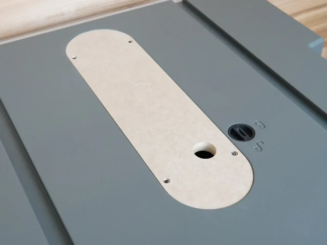 Cream-colored MDF zero clearance insert for Hercules table saw, mounted in gray table surface with center blade opening and adjustment screw holes