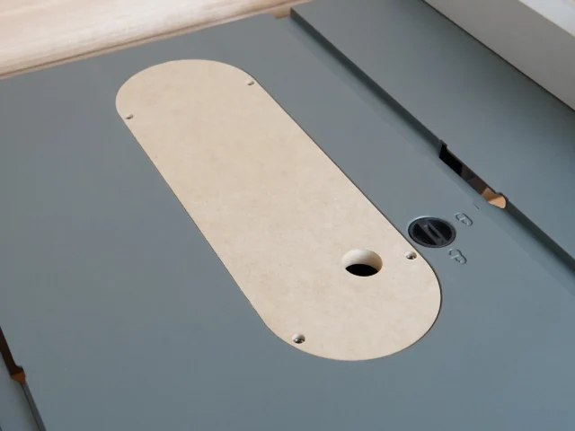 Cream MDF zero clearance insert for Craftsman CMX 10" table saw, showing oval shape with center blade slot and mounting holes, positioned on gray saw table