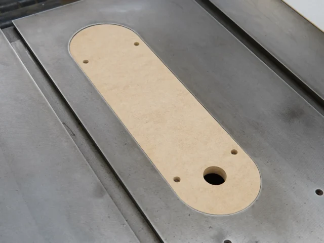 Beige MDF zero clearance insert for Delta Unisaw X5 table saw, with rounded ends and three mounting holes, shown on metal table saw surface
