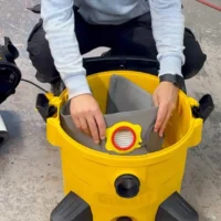 Gray polyester dust bag inserted into yellow DeWalt shop vac, held open to show filter collar with red release ring