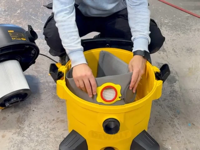 Gray polyester dust bag inserted into yellow DeWalt shop vac, held open to show filter collar with red release ring