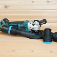Black ToolCurve 36mm hose adapter with blue band joining a hose to a Makita XAG04 grinder shroud, plus two spare adapters