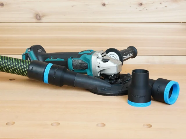 Black ToolCurve 36mm hose adapter with blue band joining a hose to a Makita XAG04 grinder shroud, plus two spare adapters