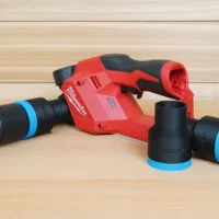 Black 36mm hose adapter with blue cuffs beside a Milwaukee M12 planer, one end joined to a vacuum hose
