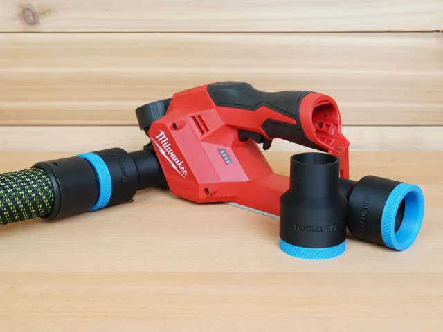 Black 36mm hose adapter with blue cuffs beside a Milwaukee M12 planer, one end joined to a vacuum hose