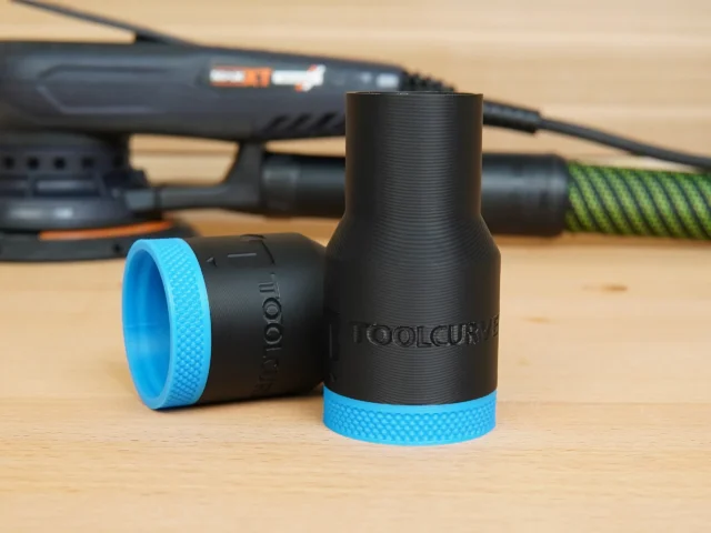 Black ToolCurve hose adapter with blue grip ring, shown with matching smaller adapter component on wooden surface behind a Festool sander