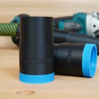 Black ToolCurve hose adapter with blue textured grip band, shown with matching adapter and Makita grinder in background