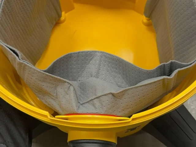 Macam reusable dust bag for DeWalt shop vacs shown inside yellow plastic housing, gray fabric interior with elastic opening visible